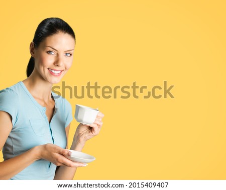 Portrait of young smiling brunette woman drinking coffee, isolated over orange yellow color background. Copy space blank area for some text or slogan. Female person at studio picture.