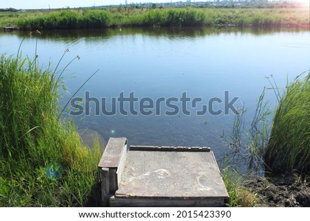 Fishing wooden bridge on the background of a pond, reeds on a sunny day. Wild nature. Fishing day concept, fishing background, wildlife, countryside vacation, camping, scouting fishing holes