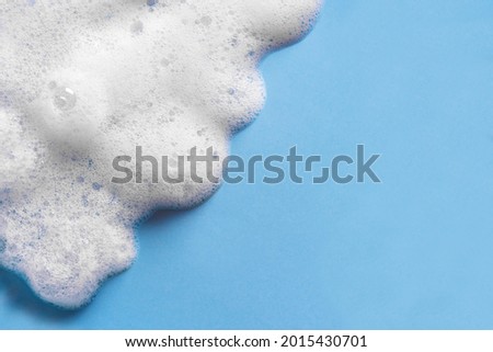 Face cleansing mousse sample. White cleanser foam bubbles on blue background, copy space. Soap, shower gel, shampoo foam texture closeup.
