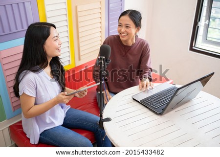 two girls laughing while chatting on a podcast using a laptop