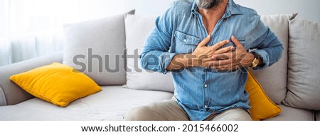 Shot of a unrecognizable man holding his chest in discomfort due to pain at home during the day. Man with chest pain suffering from heart attack while sitting at home during the day Royalty-Free Stock Photo #2015466002