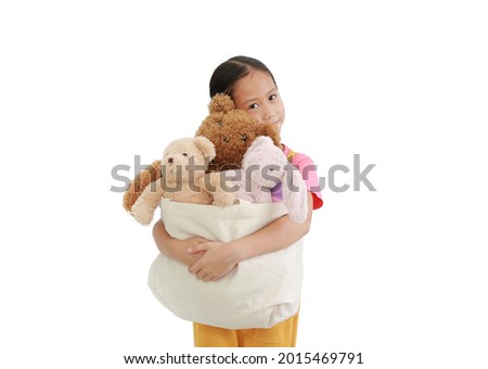 Asian little young girl hugging toys bag for donation. Kid cuddle bag of dolls isolated over white background. Concept of Pass happiness to others and sharing