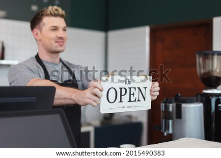 men barista holding sign wooden text open, welcome entrance shop.