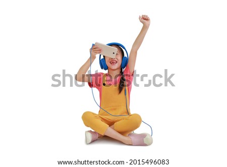 Happy Asian little girl child wearing headphones and enjoy with smartphone sitting isolated on white background. Image with Clipping path