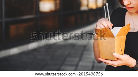 young woman or teenage girl hand eating asian fast food from takeaway box on city street. Thai noodles in paper box takeaway street food