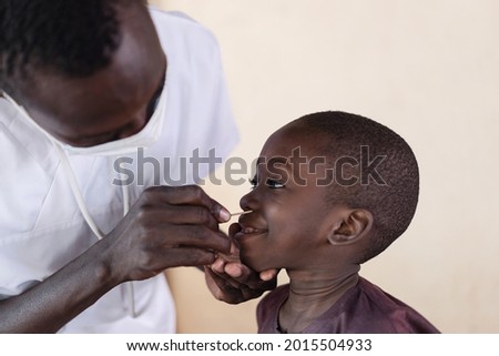 In this image a smiling little African boy is undergoing a nasal swab taken by a black nurse after a corona outbreak in a rural village