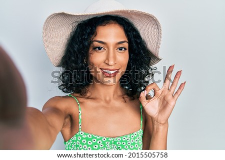 Young latin girl taking a selfie photo wearing summer style doing ok sign with fingers, smiling friendly gesturing excellent symbol 