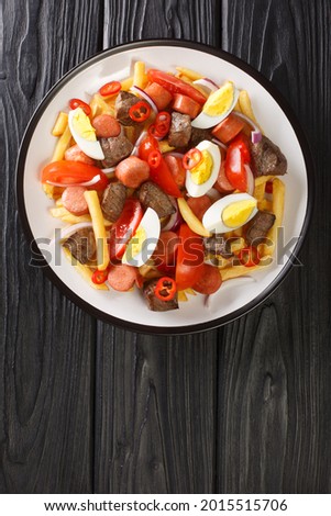 Pique macho is a typical Bolivian food consisting of pieces of beef,  french fries, onions, pepper, boiled egg closeup in the plate on the table. Vertical top view from above Royalty-Free Stock Photo #2015515706