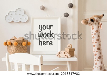 Stylish scandi child room with mock up photo frame, plush giraffe, wooden toys, boxes, blocks, wall decorations and accessories. Bright and sunny interior with wooden desk. Home decor.
