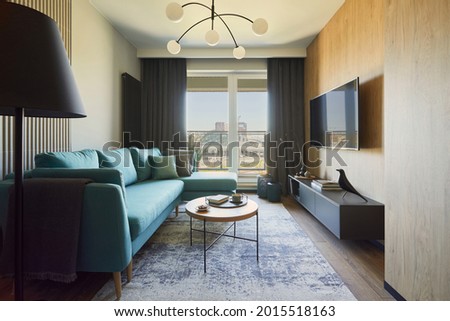 Creative composition of modern living room interior in small apartment. Eucalyptus sofa, pillows, small designed wooden coffee table, modern designed chandelier, tv and personal accessories. 