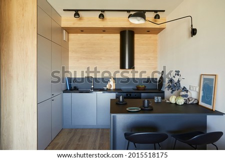 Stylish composition of modern small kitchen interior. Black furniture, workspace and dining space with black and light wooden kitchen accessories. Wooden panel creative walls. Minimalist concept.