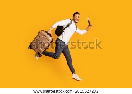 Portrait Of Young Happy Arab Man Jumping With Suitcase And Pasport, Ready For Vacation Trip, Excited Middle Eastern Guy Running With Luggage Over Yellow Background, Full Length Shot, Copy Space Royalty-Free Stock Photo #2015527292