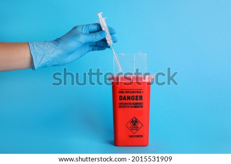 Doctor throwing used syringe into sharps container on light blue background, closeup Royalty-Free Stock Photo #2015531909