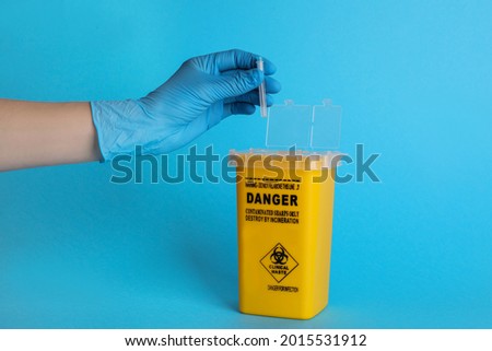 Doctor throwing used syringe needle into sharps container on light blue background, closeup Royalty-Free Stock Photo #2015531912