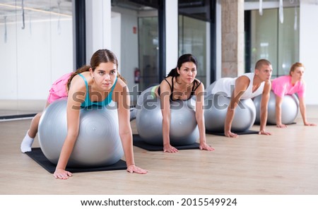 Adult sports people practiciting Pilates in the studio during a group training session perform an exercise on a fitness ball, ..which strengthens the lumbar region and develops overall flexibility Royalty-Free Stock Photo #2015549924