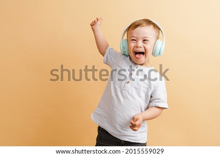White boy with down syndrome in headphones laughing at camera isolated over beige background Royalty-Free Stock Photo #2015559029