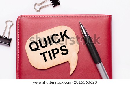 On a light background there are black paper clips, a pen, a burgundy notepad a wooden board with the text QUICK TIPS