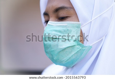 A women wearing hijab using single surgical face mask isolated with white background. The face mask will protect us from covid19 corona virus during pandemic.