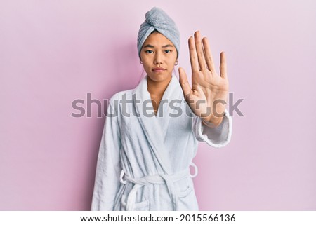 Young chinese woman wearing shower towel cap and bathrobe doing stop sing with palm of the hand. warning expression with negative and serious gesture on the face. 