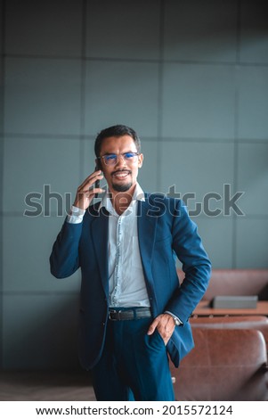 Smiling businessman using smartphone to call secretary happily at work