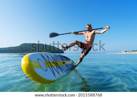 A man learns to stand on a board and falls into the water from a large yellow paddle board. Royalty-Free Stock Photo #2015588768