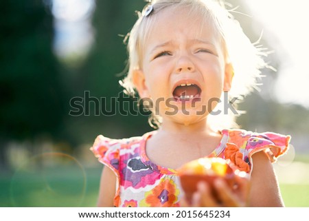 Little girl whimpers holding a peach in her hand. Close-up Royalty-Free Stock Photo #2015645234