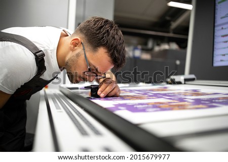 Worker checking print quality of graphics in modern printing house. Royalty-Free Stock Photo #2015679977