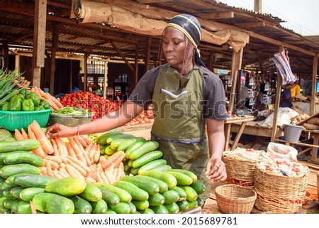 stock photo of female African grocery seller or business woman with apron, standing at her stall in a market, ready to sell to customers