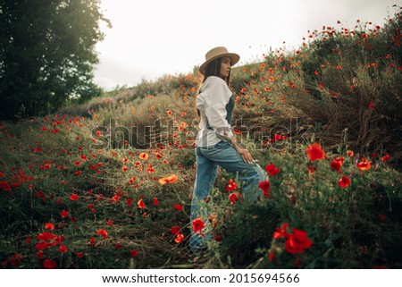 Young woman in straw hat enjoys by flowering poppies among meadow.