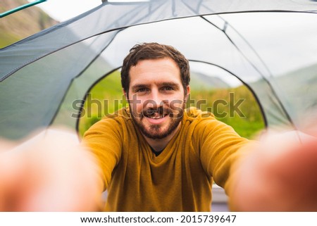 Photo of a young and attractive man taking a selfie inside a tent outdoors. Happy to do solo camping
