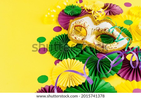 Colorful paper confetti, carnivale mask and colored serpentine on a yellow background with copy space, greeting card and party invitation template design for carnival or birthday, Mardi Gras,