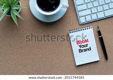 BOOST YOUR BRAND text with notepad, keyboard, decorative plant, coffee cups and fountain pen on wooden background. Technology, Business and copy space concept

