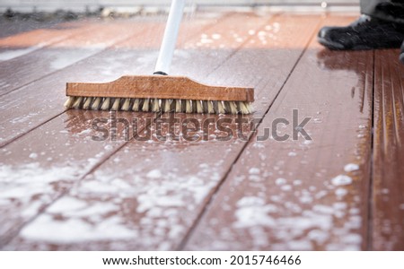 Detail of a scrubbing brush during spring cleaning on a wooden terrace with soap and splashes of water