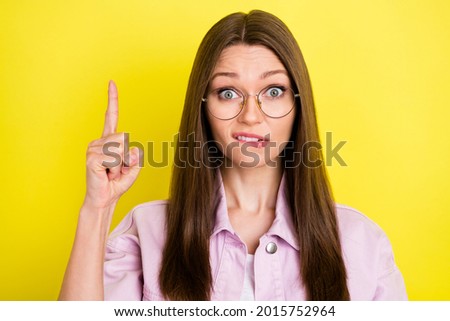 Photo portrait young woman pointing finger up blank space biting lip stressed got trouble isolated vivid yellow color background