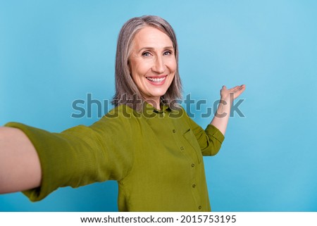 Photo of positive lady make selfie palm invite presenting empty space wear green shirt isolated blue color background