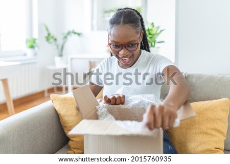 Happy young woman sit on couch in living room unpack cardboard box buying goods on Internet, smiling excited millennial girl open carton parcel order, shopping online, good delivery concept