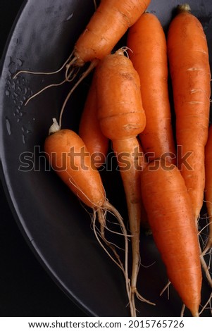 Fresh carrots in black plate on a black background. Top view.