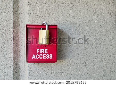 Red fire access box with padlock on a plain textured wall with copy space.