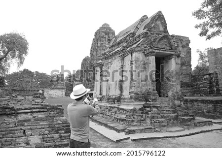 Monochrome image of a visitor photographing the remains of Wat Mahathat temple in Ayutthaya Historical Park, Thailand