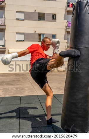 Young caucasian man kicking a punching bag hanging on the street, he trains hard to improve. Contact sport. Training concept