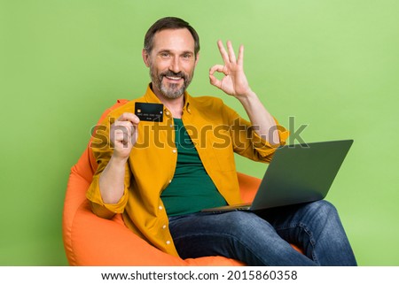 Profile side photo of mature man happy smile show okay alright sign pay credit card online laptop isolated over green color background
