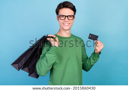 Photo portrait young guy smiling wearing green pullover glasses showing bank card on shopping isolated pastel blue color background