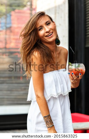 Elegant fashionable brunette woman drinking alcoholic tasty cocktail and having fun, wearing cute white beach dress and trendy accessorizes . Royalty-Free Stock Photo #2015863325