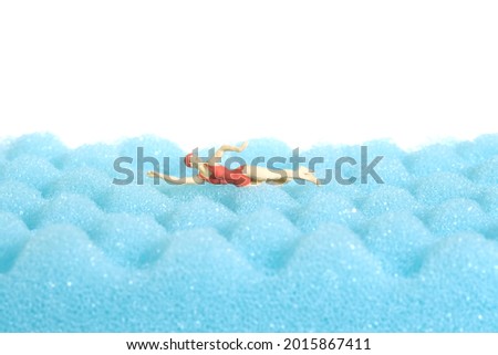 Miniature people toy figure photography. Swimming water sport. A young women freestyle swimmer above blue foam with wave pattern, isolated white background. Image photo