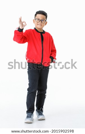 Funny cutout portrait of smart young healthy Asian boy on red jacket happily miling and raising right hand up to show OK sign as satisfying, confident, trust, ensure something and not worry