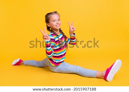 Photo of little girl make twine show two v-signs wear striped shirt jeans sneakers isolated yellow color background