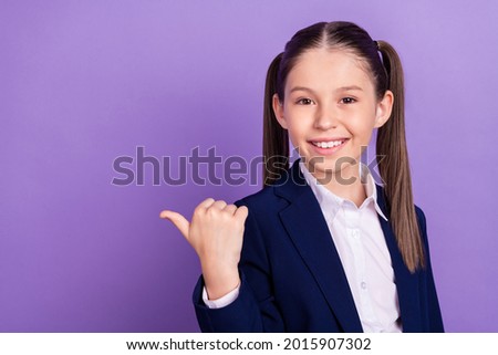 Photo of shiny pretty schoolgirl dressed blue uniform smiling pointing thumb empty space isolated violet color background
