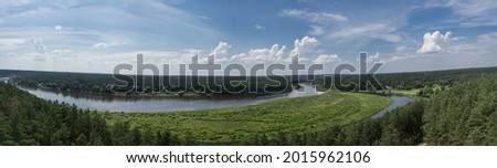 Panoramic view from the top of Merkine observation tower onto Nemunas river and surrounding riverbanks covered with green forest. Warm summer day. White clouds in blue sky.