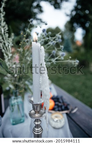 vertical photo of a gray burning candle with a lot of wax against the backdrop of flowers