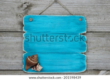Blank wood sign with seashells hanging on antique rustic wooden background; beach background with teal blue copy space